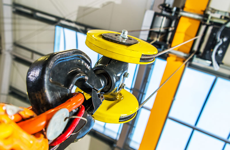 Close-up of a heavy-duty industrial crane hook and pulley system, with cables attached, inside a brightly lit warehouse specialising in rope access manufacturing in South Africa. - OADR Training